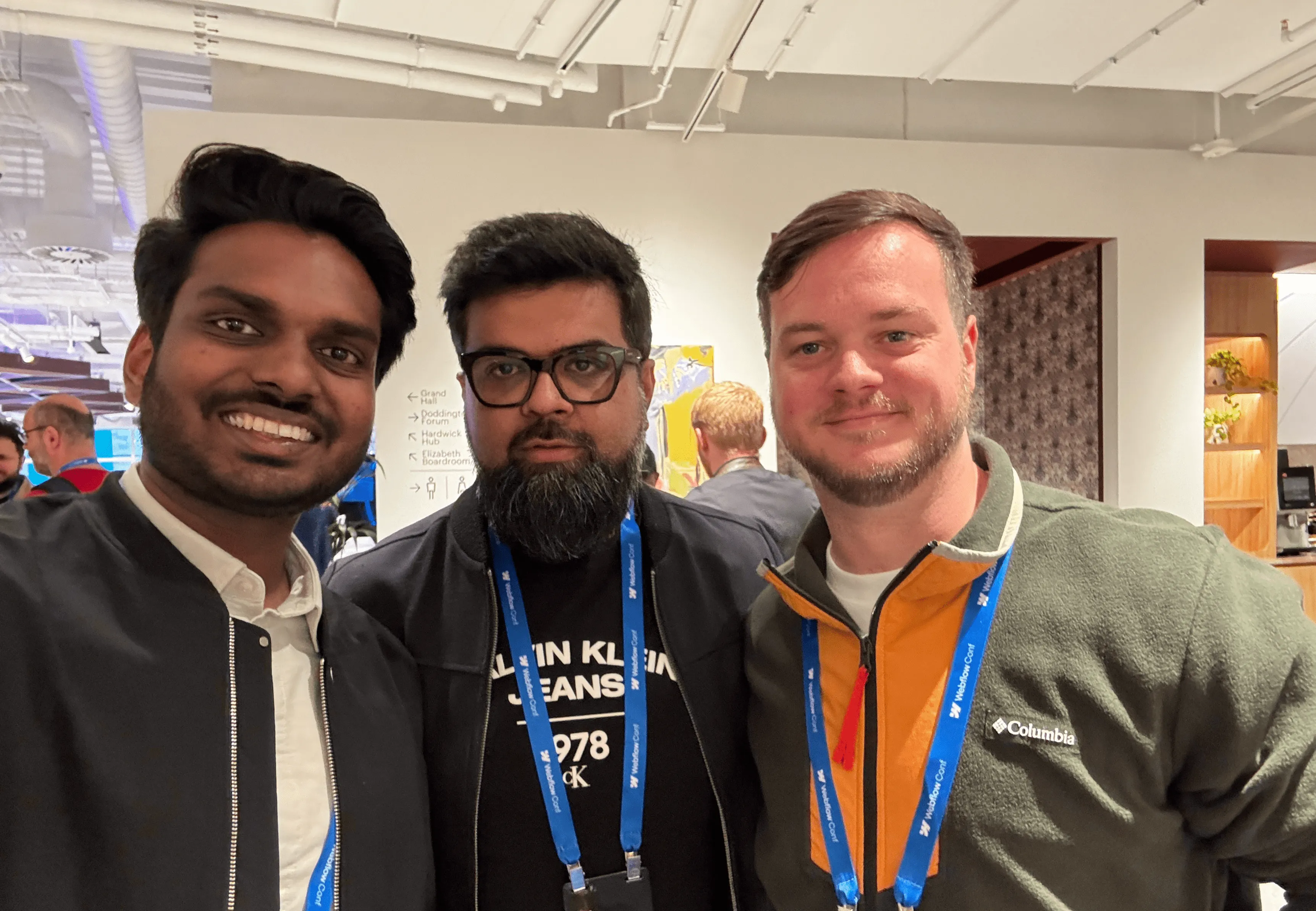 Three men wearing event lanyards smiling and posing for a photo indoors.