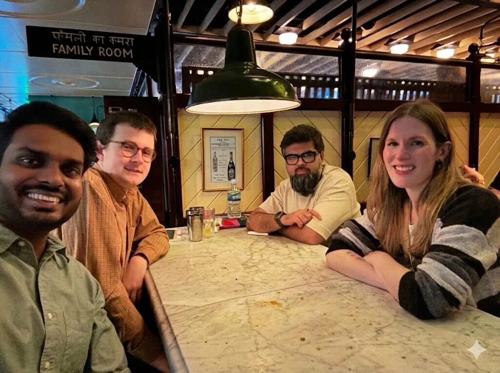 Four people smiling and sitting around a marble table in a warmly lit room with a 'Family Room' sign in Hindi and English.