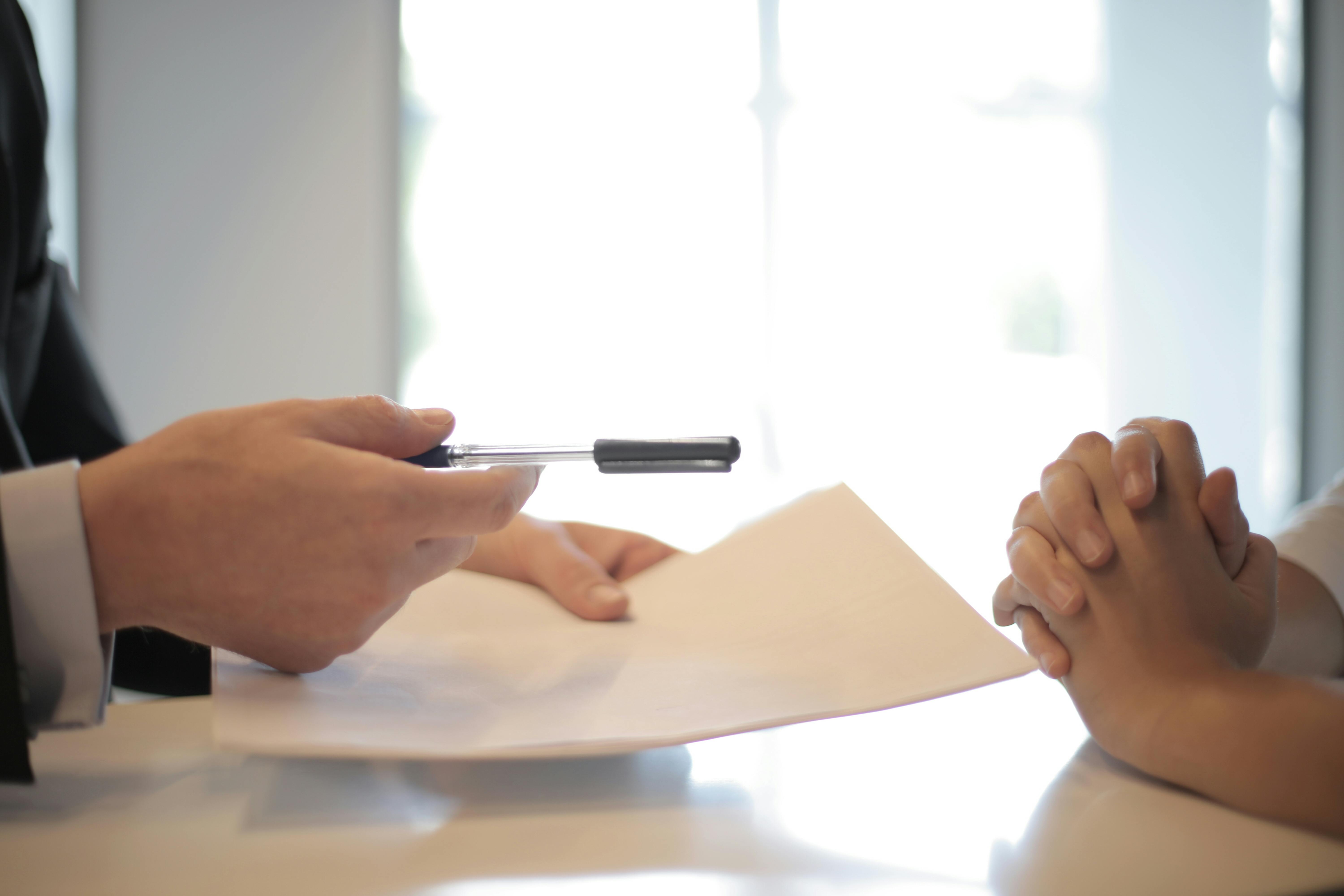 a man handing some one a pen and paper to fill out and sign