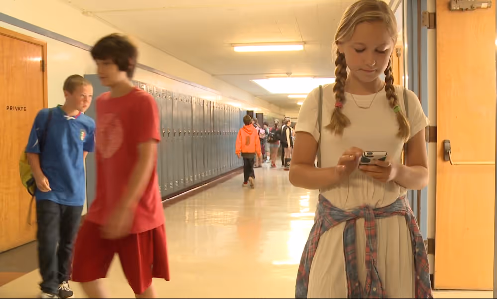 Girl using phone with 2 boys in background in school lobby