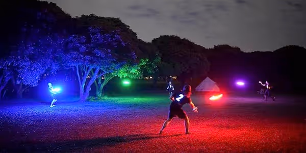 3 people playing with bright light up frisbees at night in a dark park.