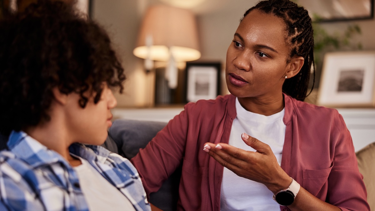 Mother talks with her teen son on the sofa.