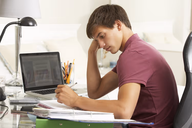 A young man holding a pen and looking at a screen