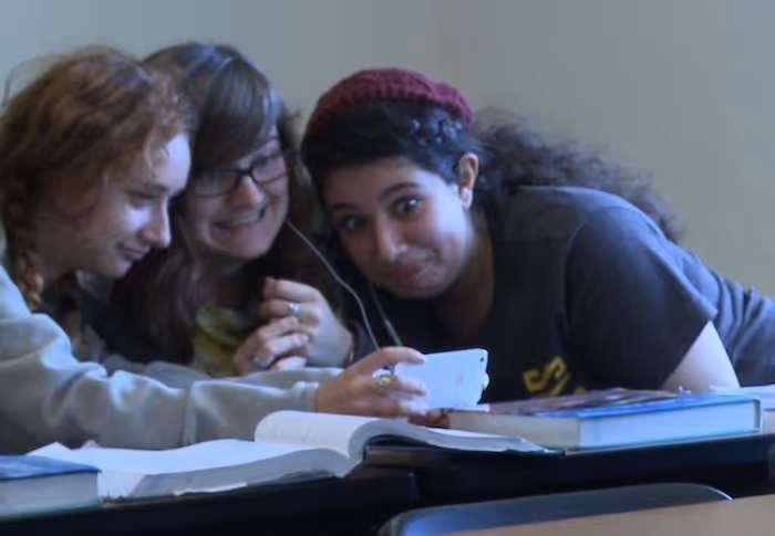Three females are watching something really interesting on an iPhone  