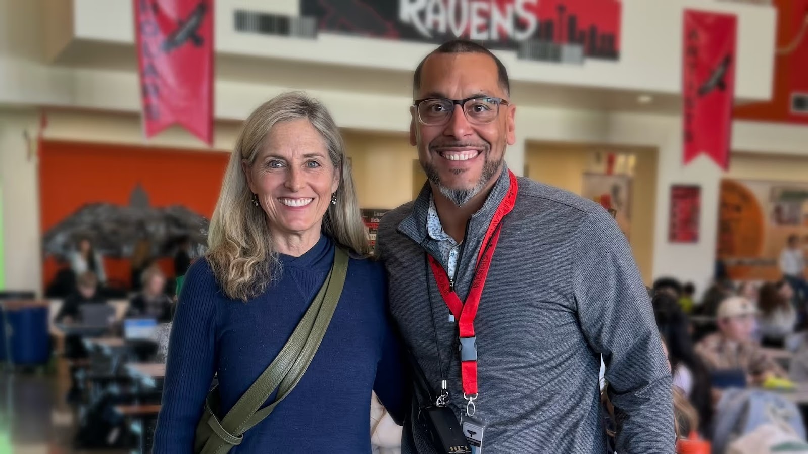A middle age woman and man, smiling for the camera in a high school cafeteria.