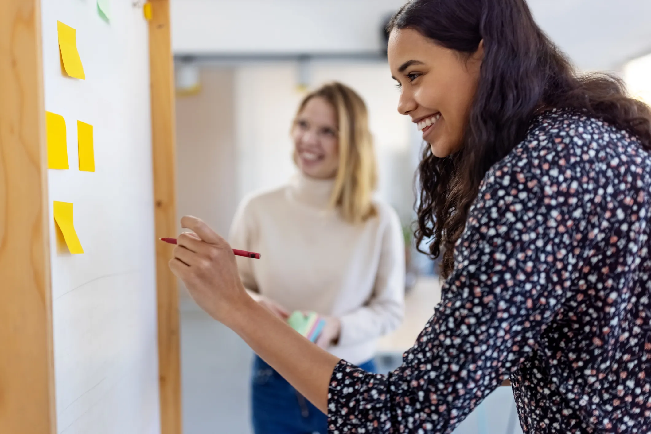Two women brainstorming with sitcky notes and a white board