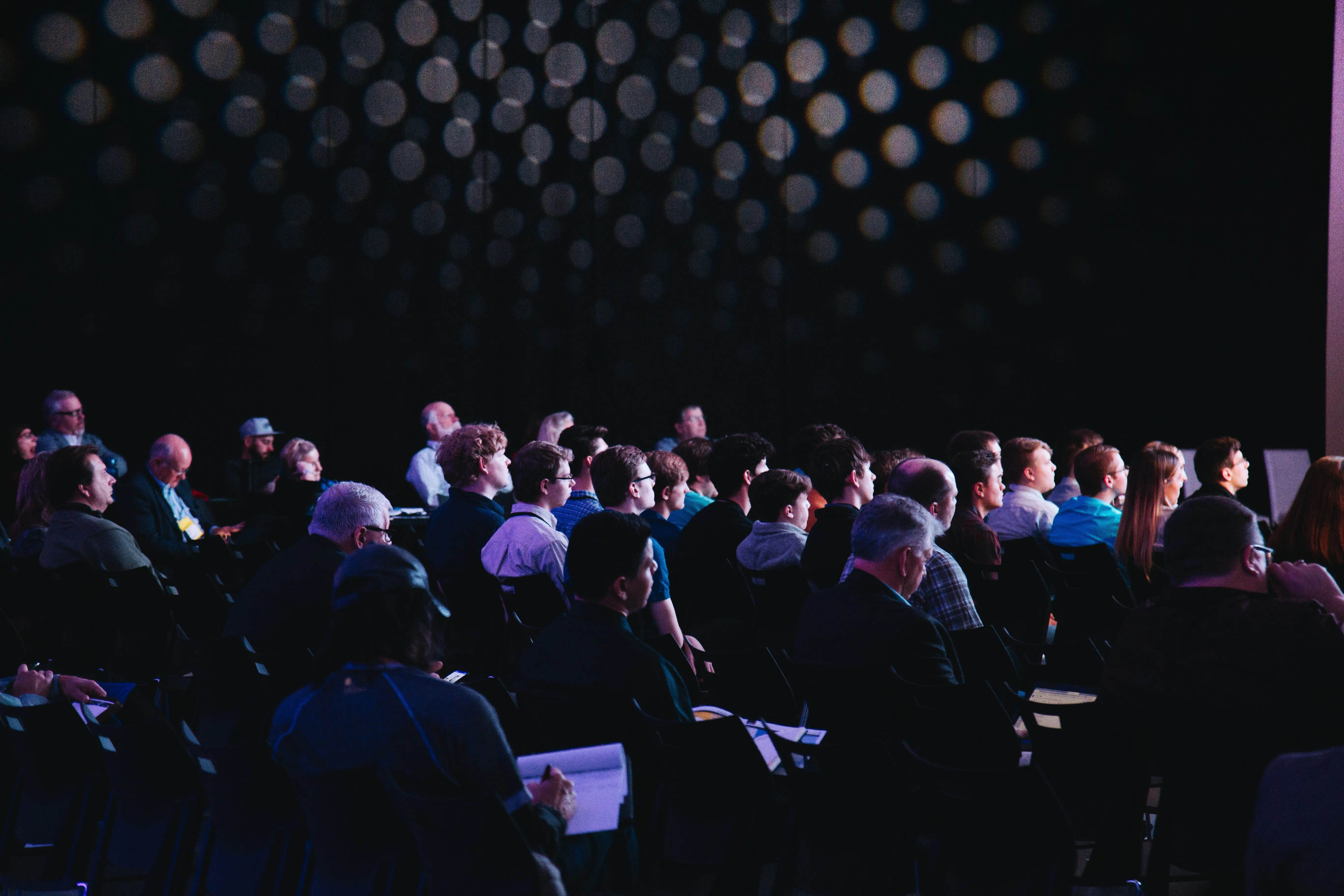 Room full of people sitting in chairs. View is of the backs and sides of their heads