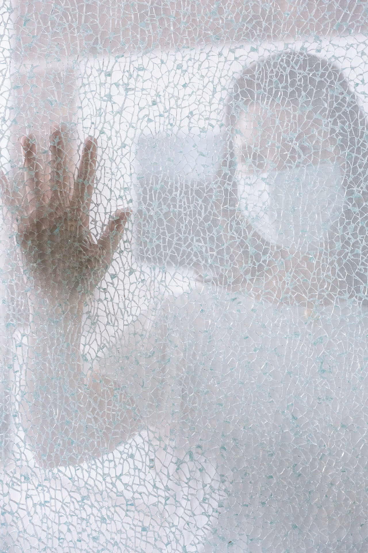 Osoba viděná skrz strukturovanou průsvitnou záclonu s jednou rukou přitisknutou k ní.