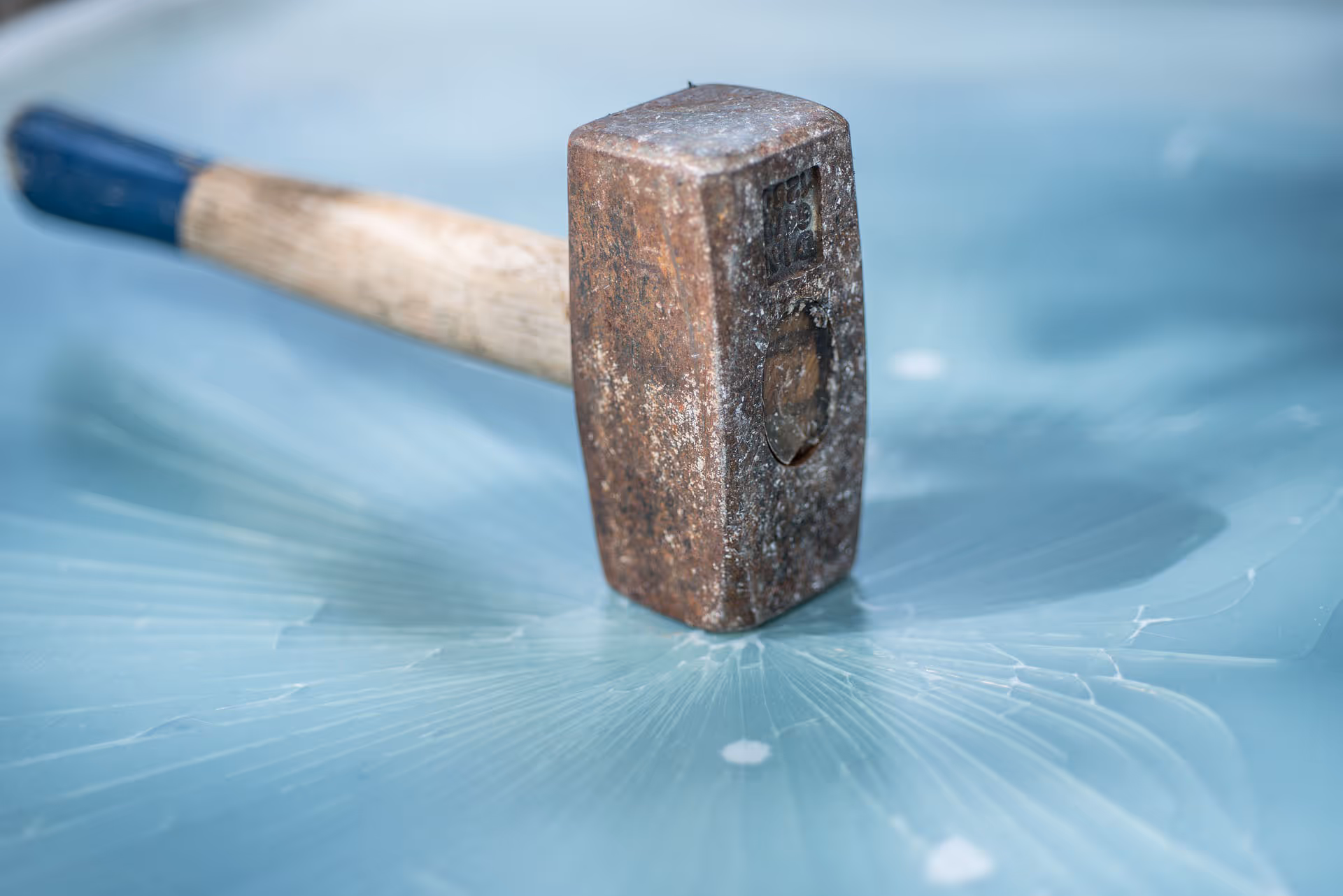 Rezavé kladivo ležící na popraskaném modrém povrchu s paprskovitými trhlinami.