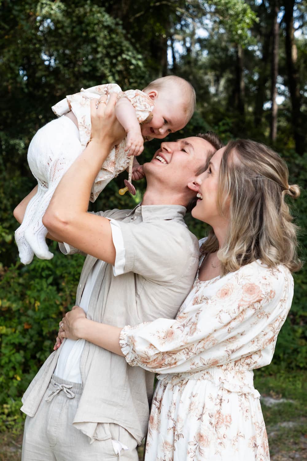 A husband and wife hugging and holding up their baby