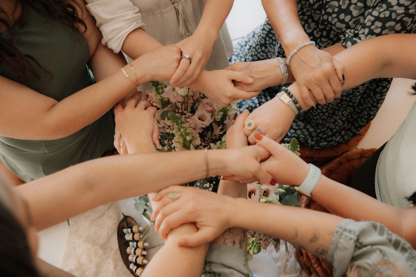Frauen halten sich im Kreis an den Händen, in der Mitte Blumen und Öle