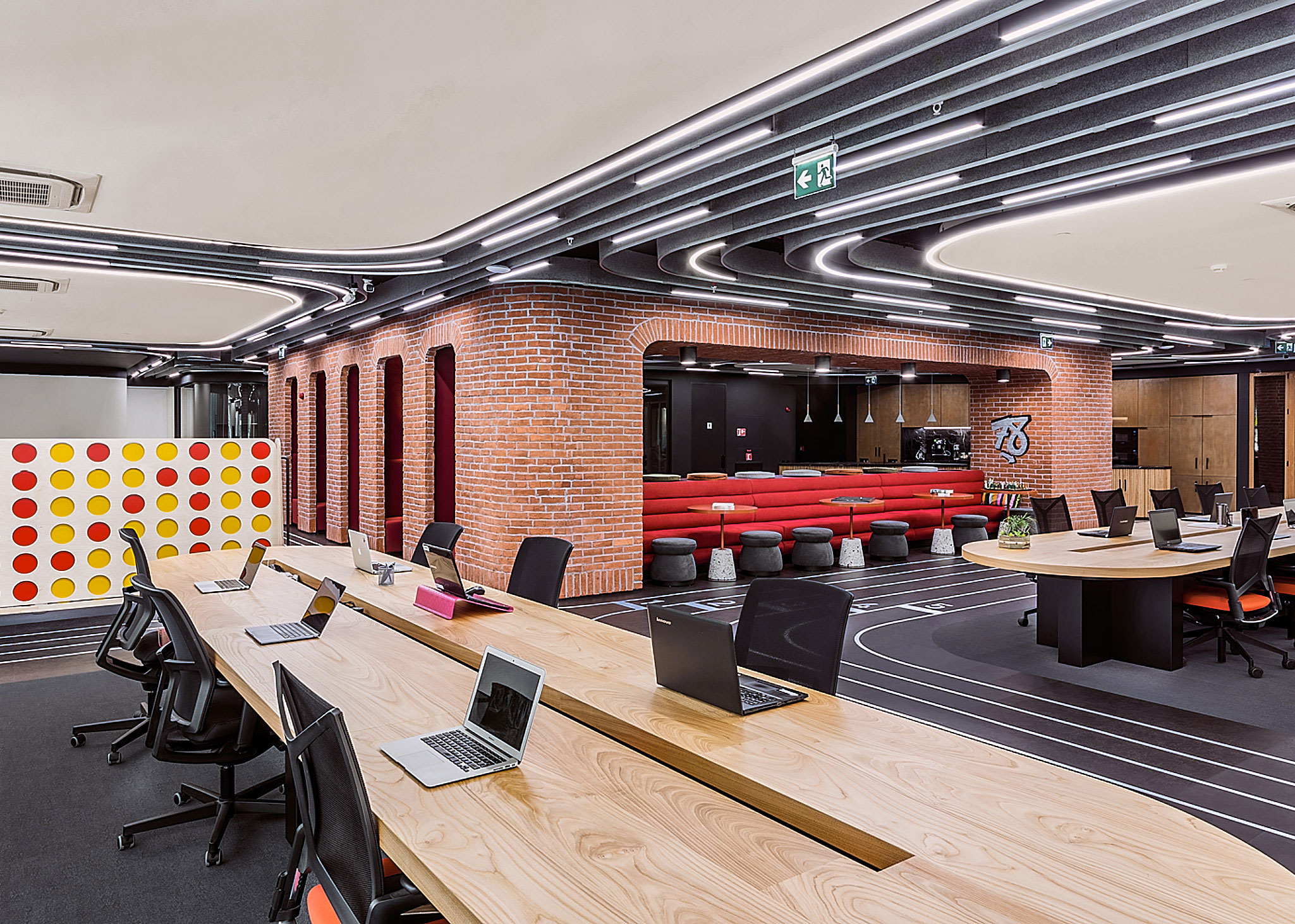 Open workspace with long shared desks, acoustic ceiling baffles, and a playful "Connect 4" game inspired room divider.
