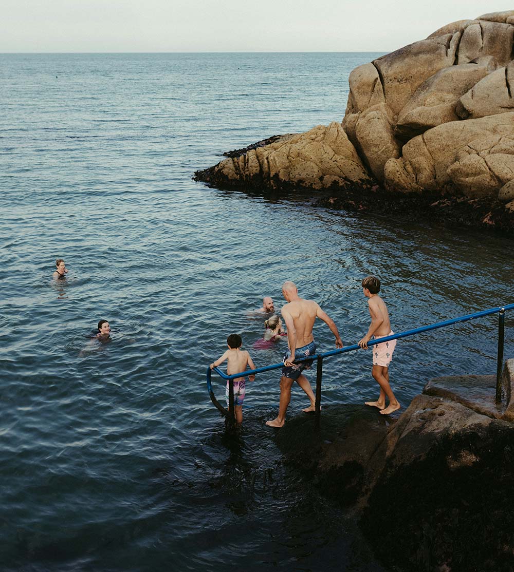 A family steps carefully down rocky stairs into the ocean while others swim nearby, reflecting how insurance planning provides security for life’s adventures