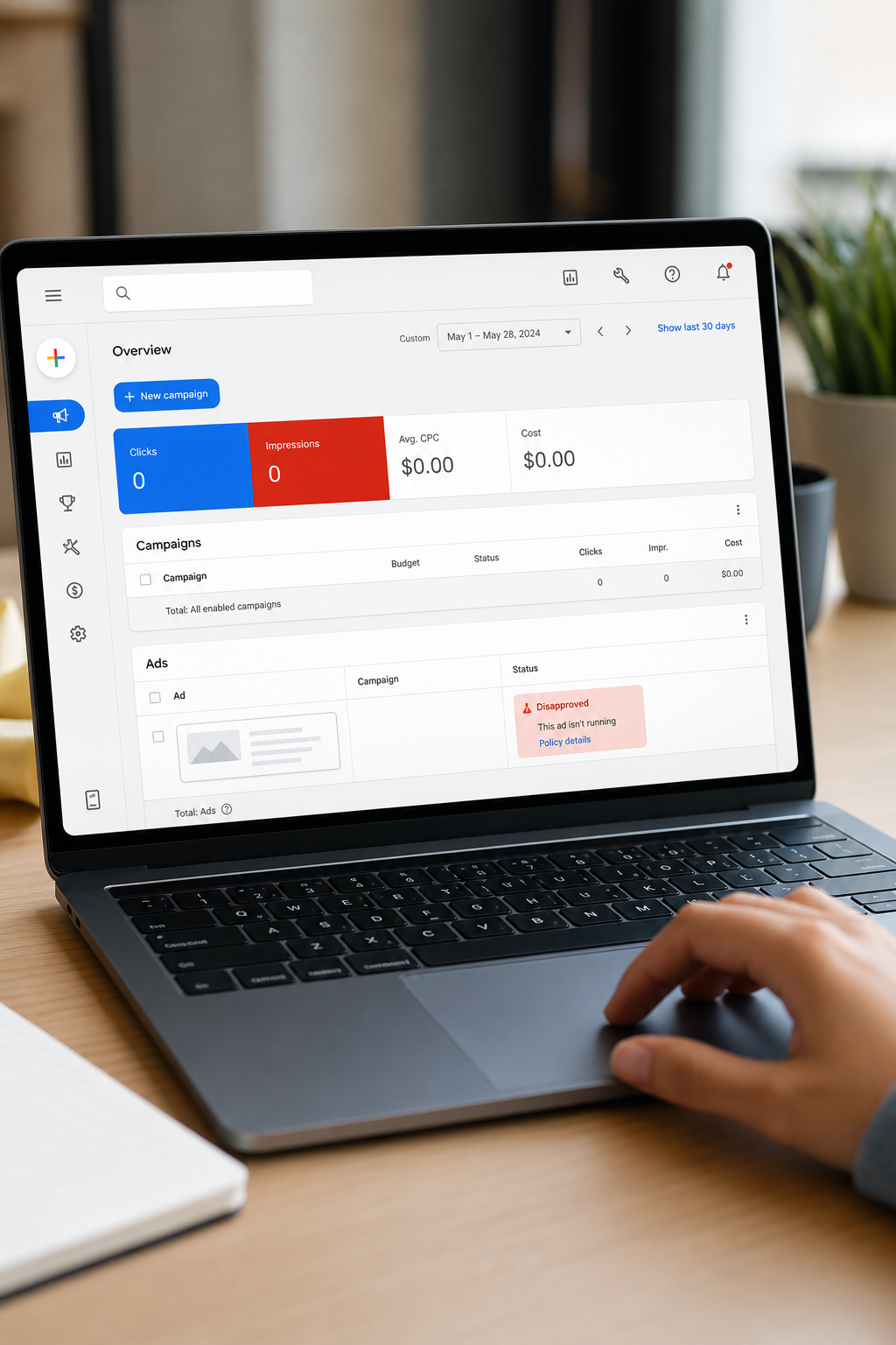 A realistic close-up of a laptop screen showing a Google Ads dashboard with a disapproved ad status highlighted in red, a person's hand hovering near the trackpad in a modern office setting. Alt: Google Ads dashboard showing disapproved ad status notification.