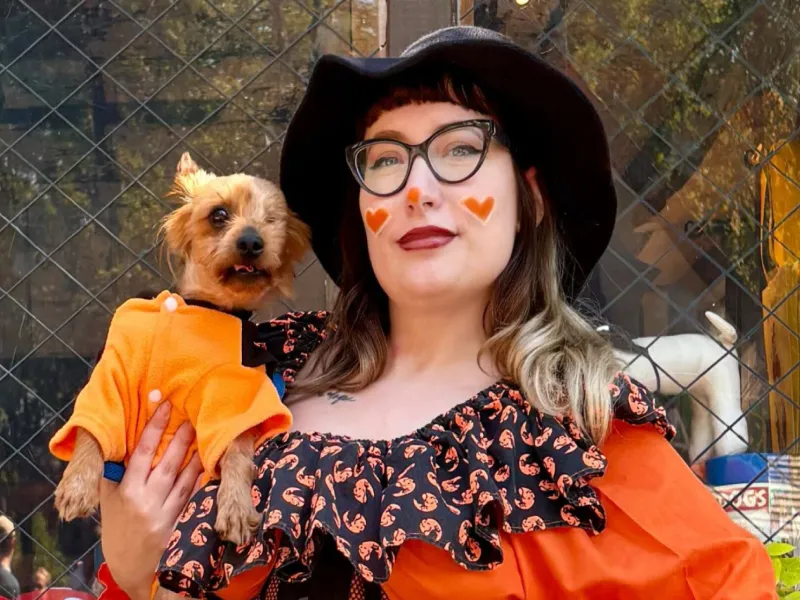 A woman dressed up for Halloween with a small dog in costume