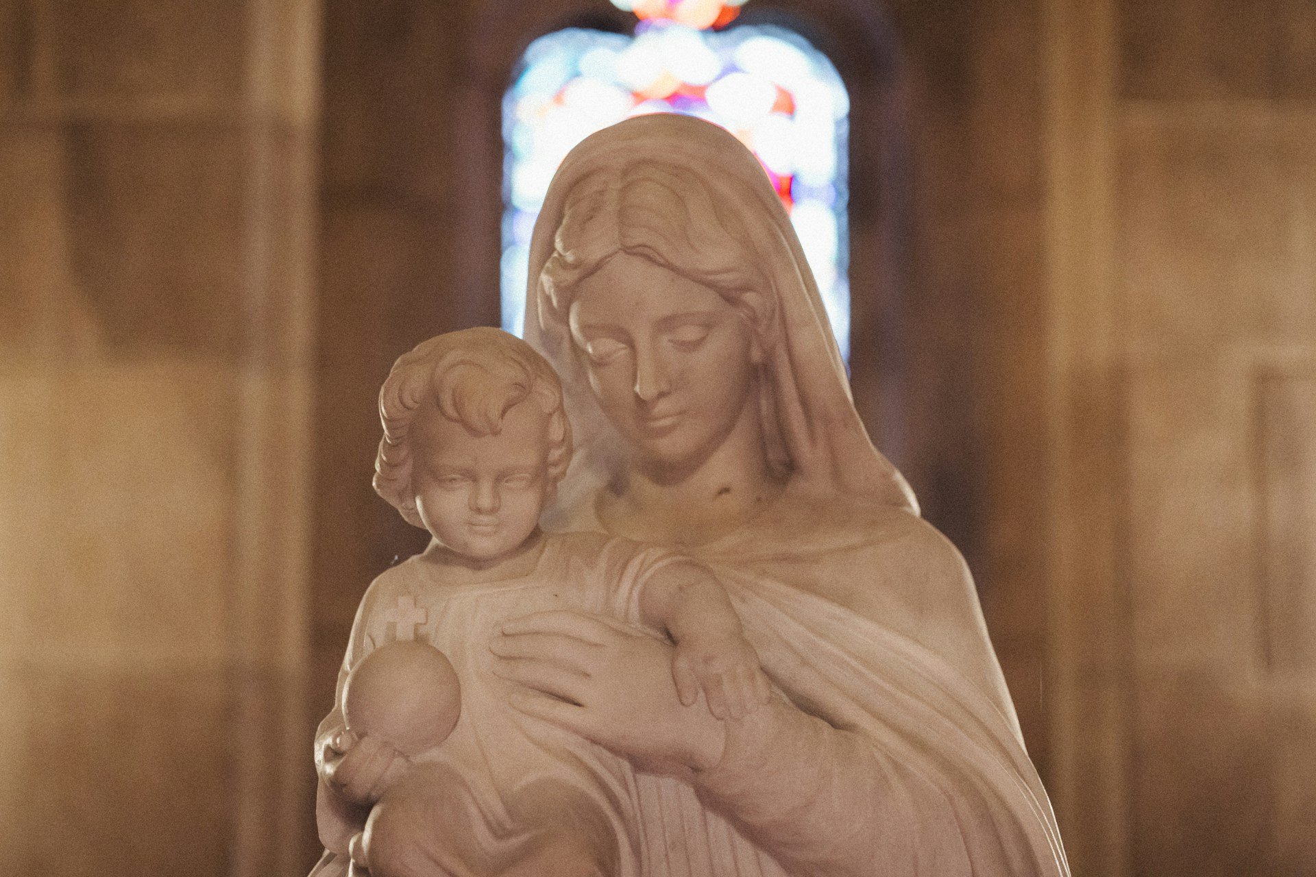 Marble statue of Our Lady holding the Christ Child before a stained glass window