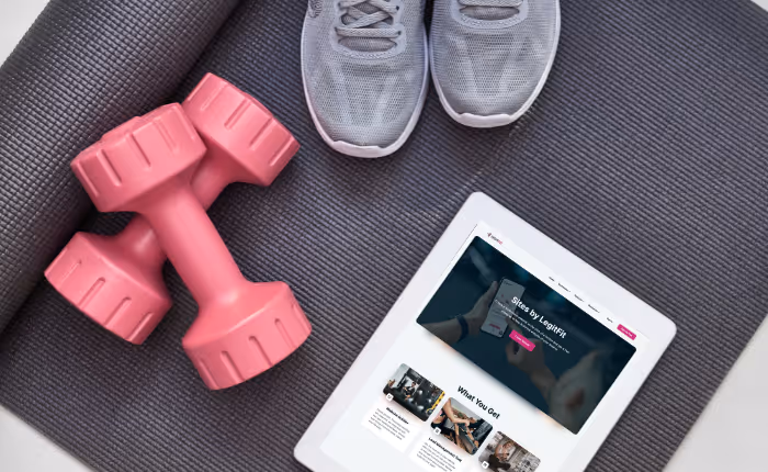 top view of an exercise grey mat half rolled up with these items on top: pink weights, light grey shoes and a white tablet with Sites page displaying on screen.