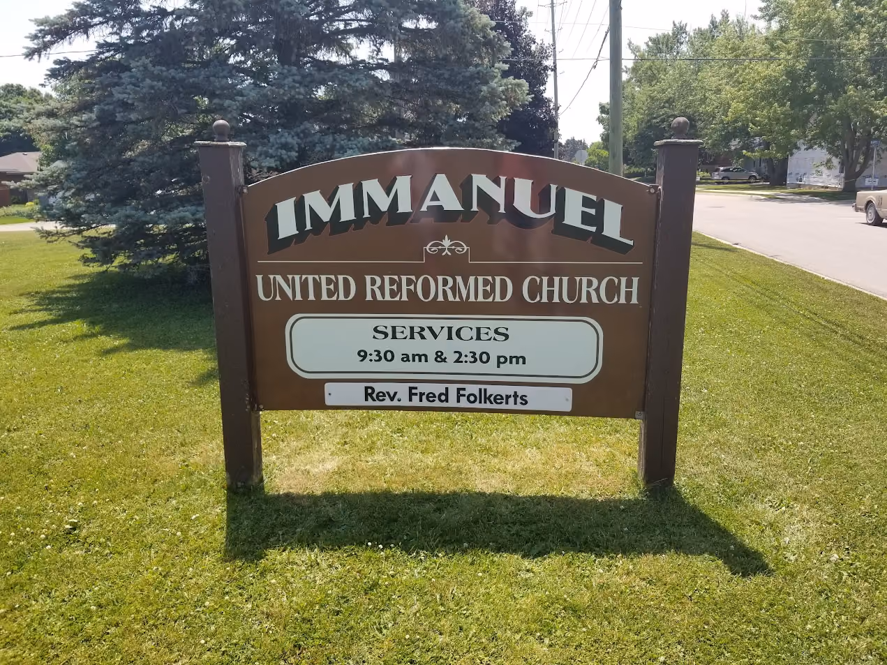 A church sign reads "IMMANUEL UNITED REFORMED CHURCH" with service times at "9:30 am & 2:30 pm" and "Rev. Fred Folkerts." It's set on a grassy area by a street.