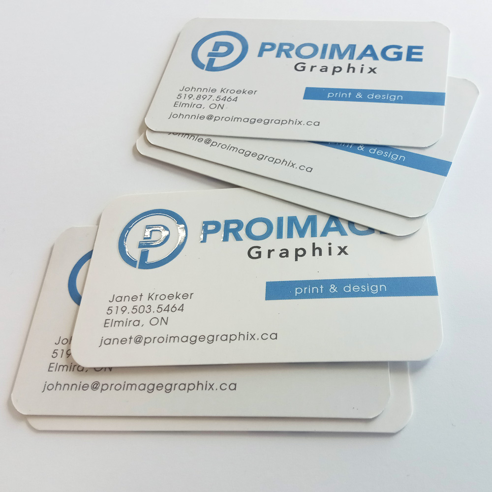 Business cards with blue and black text on a white background display company name "PROIMAGE Graphix," contact details for Johnnie and Janet Kroeker, and a "print & design" tagline, stacked casually.