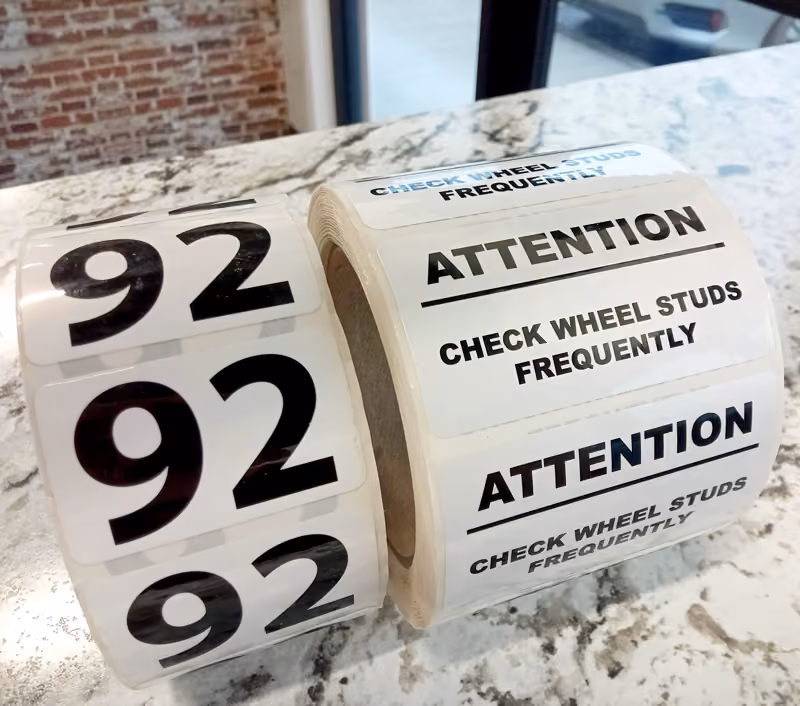 Photo of OEM Labels on a roll with numbers "92" and wording "Attention. Check wheel studs frequently"