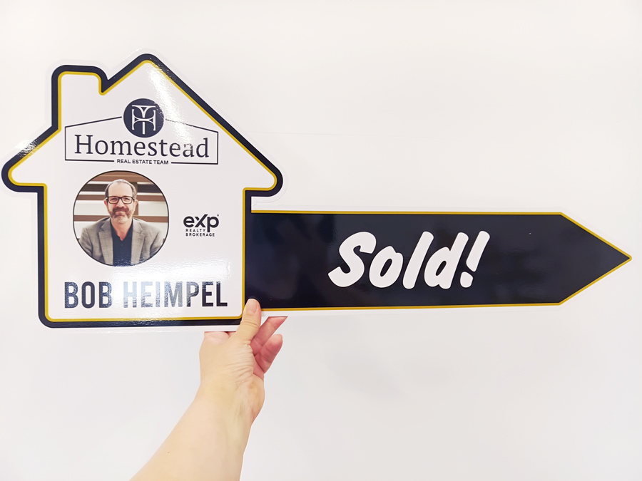 Photo of a sign cut in a shape of the house with a right arrow, "Sold!" and Homestead Real Estate Team branding