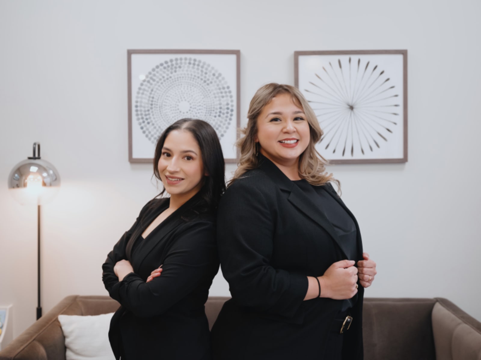 Two female dental professionals in black uniforms posed together in office