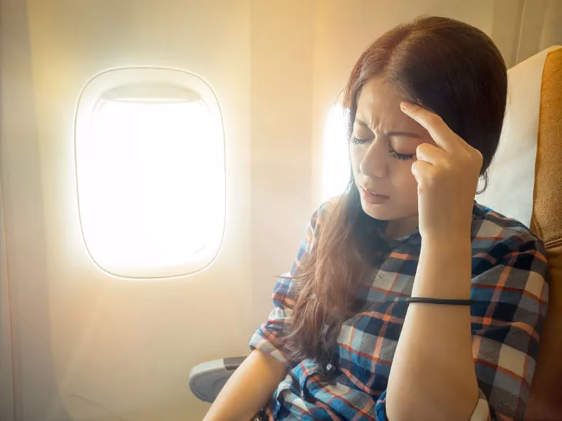 Person seated by airplane window with sunlight streaming in.