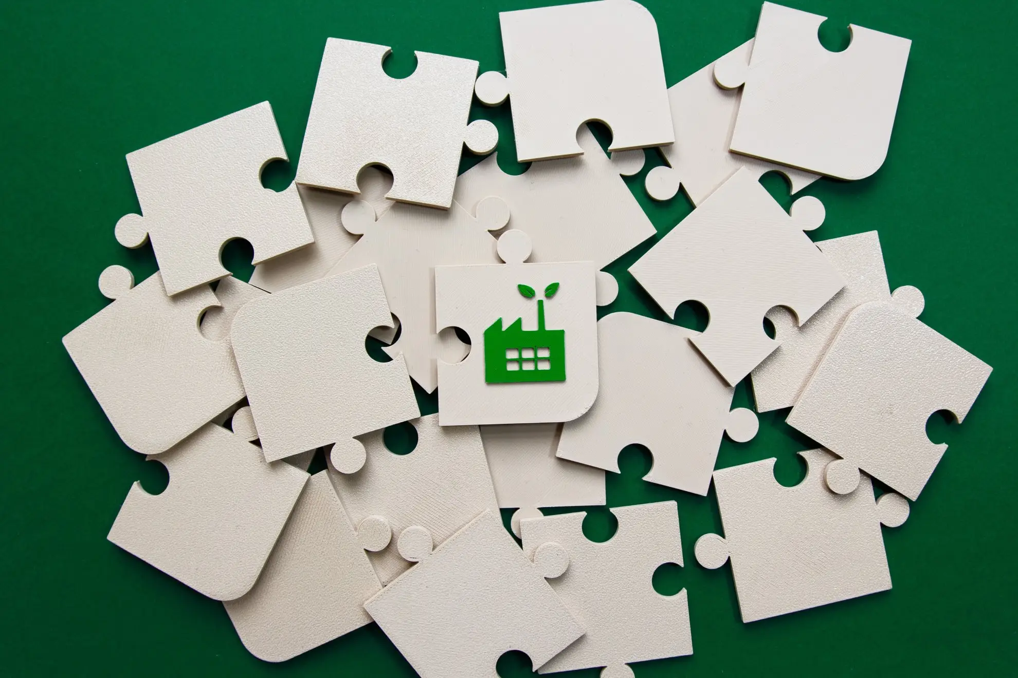 Viele Puzzleteile auf grünem Hintergrund. Es handelt sich um Blanko-Teile mit einer Ausnahme. Auf dieser ist ein Icon zu sehen, das als Symbol für nachhaltige Wirtschaft gelten kann.