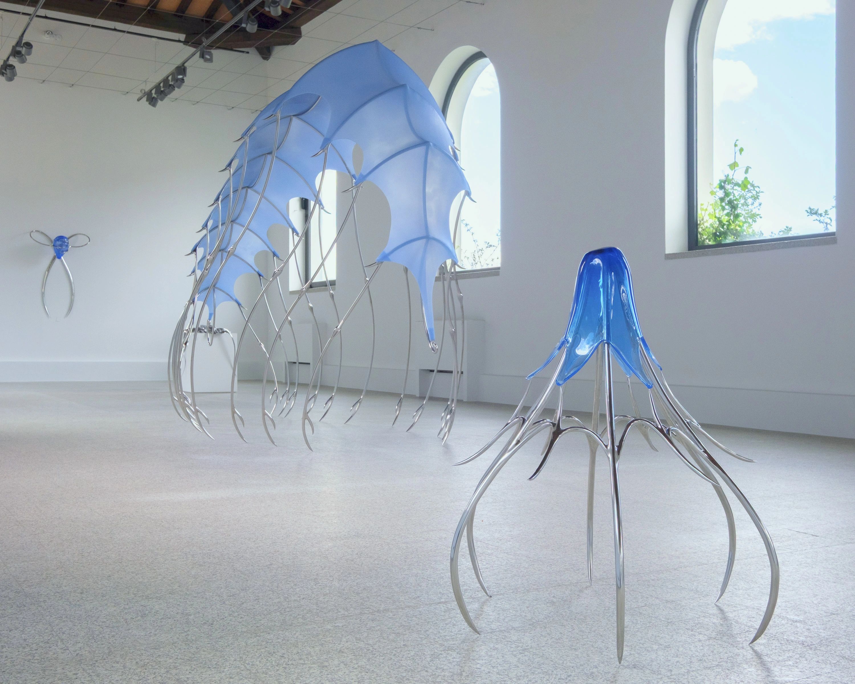 Hannah Levy, a freestanding blown cobalt-glass lamp-form nestled inside a cage of splayed hooked steel legs in foreground, the silicone canopy visible in the background
