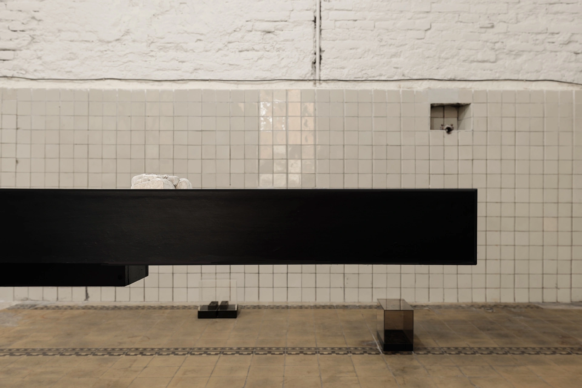 Sofiia Yesakova, black dissection table edge detail with white plaster object resting on surface, white tile wall behind, 2026