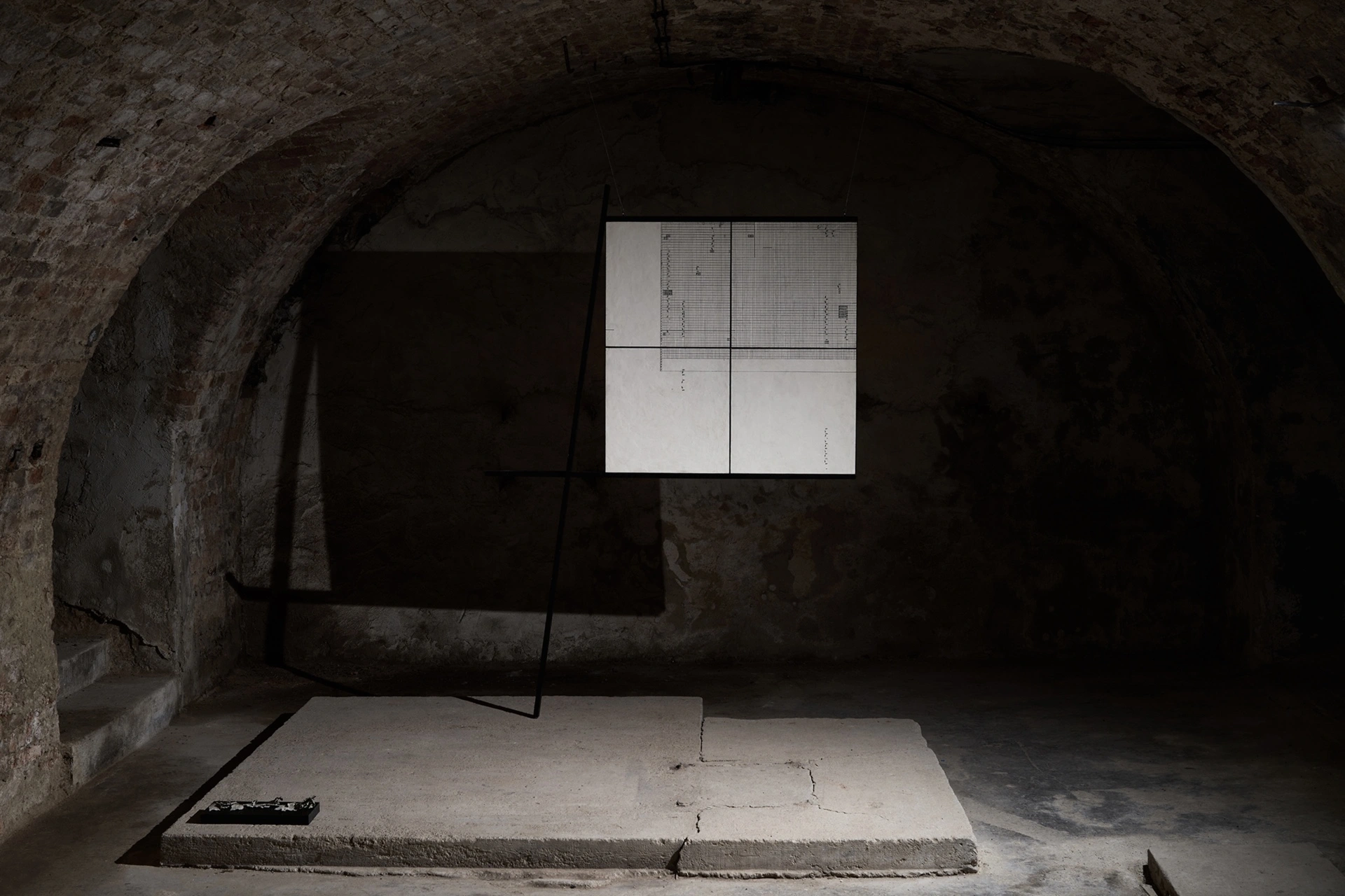 Installation view, lower vaulted space at FAVU Gallery with Anzhelika Palyvoda's grid panel on easel stand, stone floor, 2026