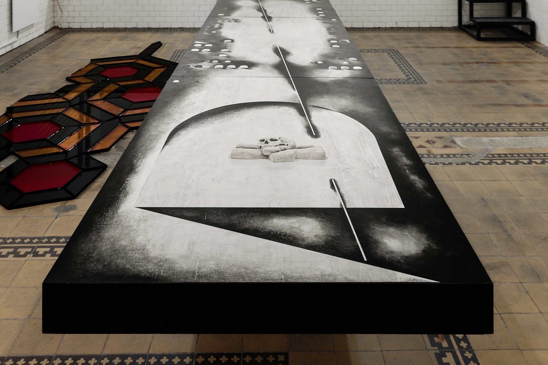 Sofiia Yesakova, panoramic view of dissection table surface showing charcoal painted scalpels, skull, and smoke-cloud anatomy, Céline Struger hexagonal grid to left, 2026