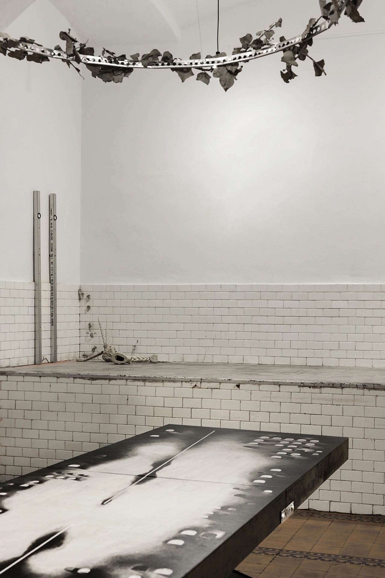 Installation view, main hall with Sofiia Yesakova's black dissection table and Céline Struger's chandelier wreath above, 2026