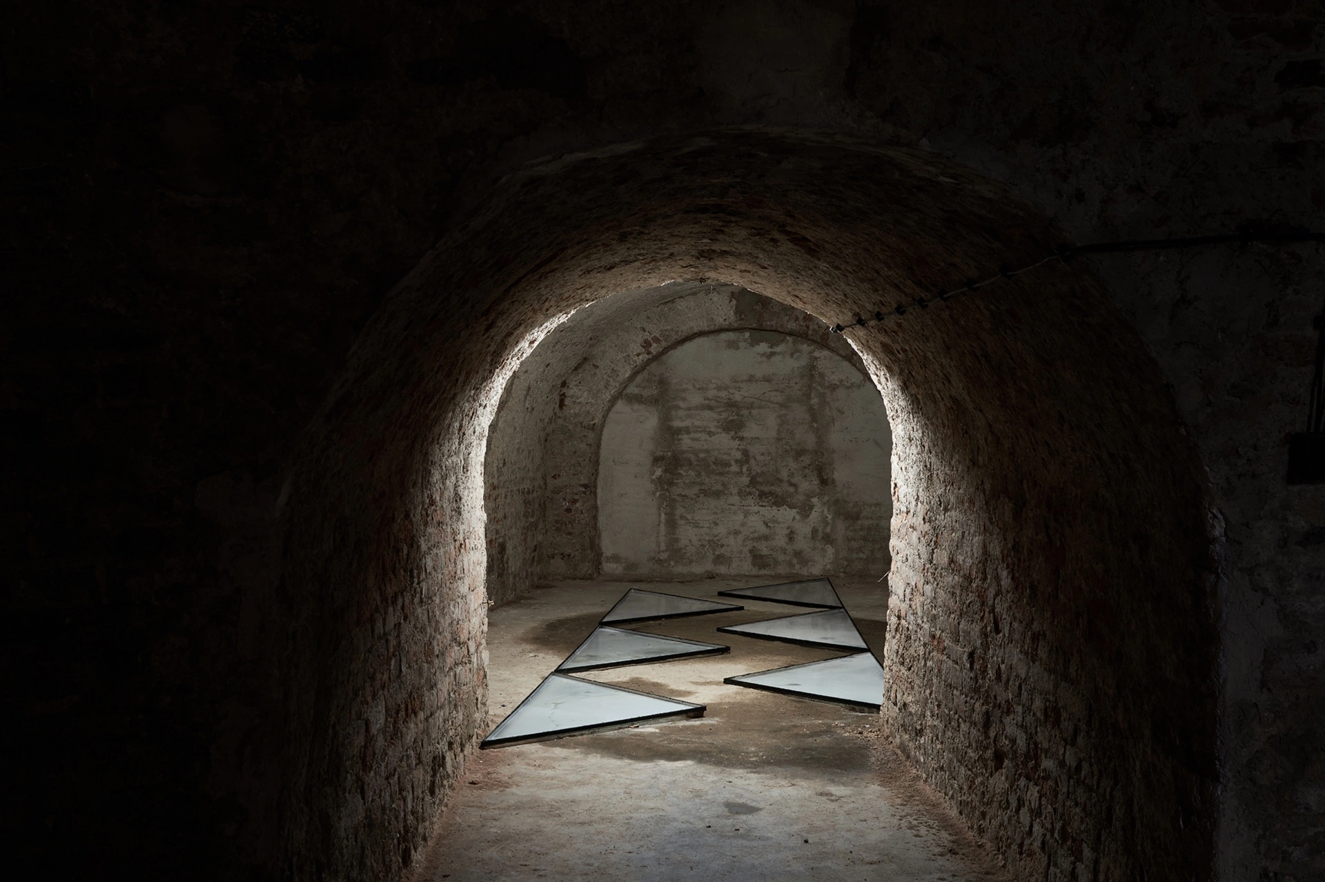 Anzhelika Palyvoda, triangular mirror panels arranged on floor of vaulted underground passage, FAVU Gallery, 2026