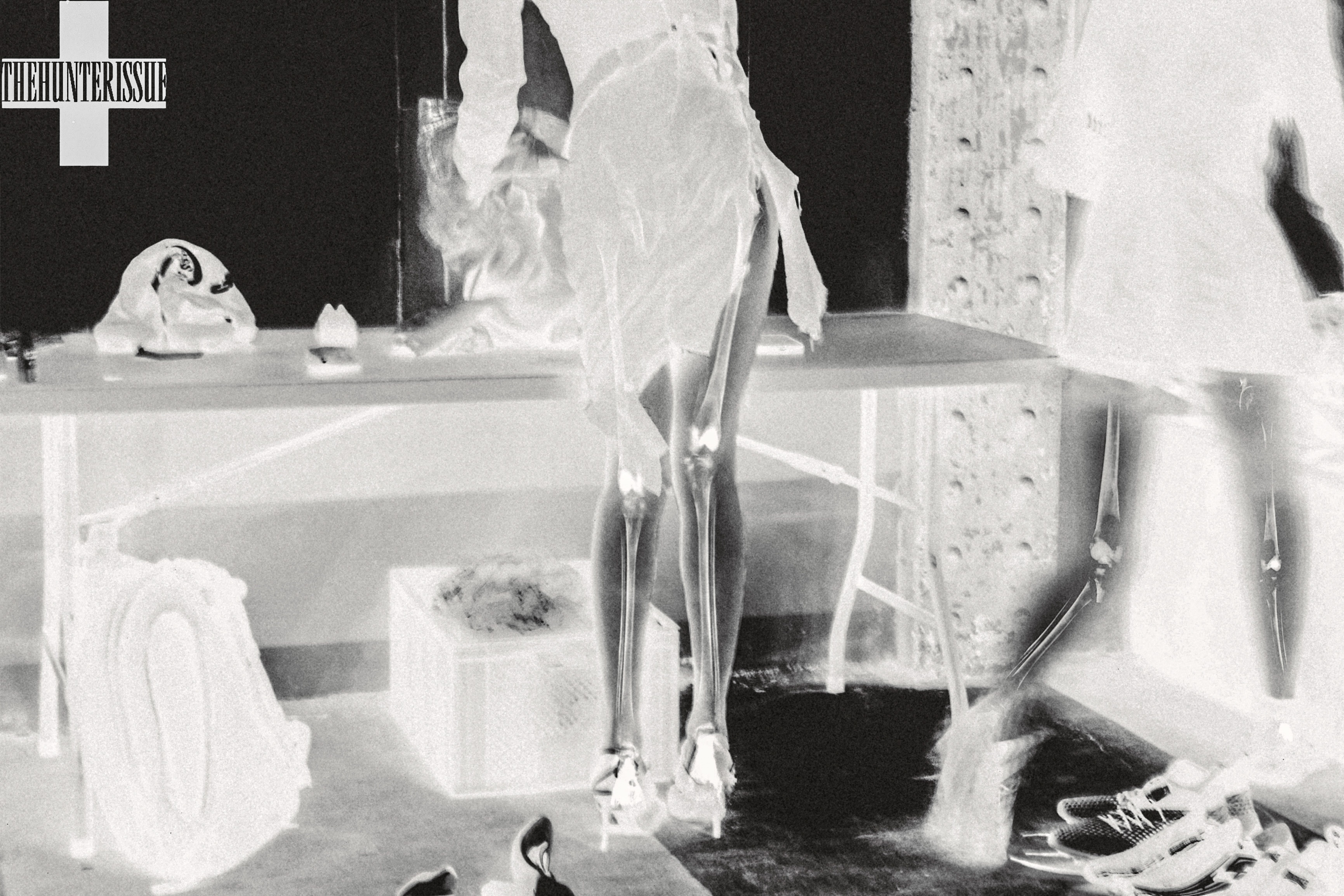 Spread from TheHunterIssue Vol.1 by Leo Shmunk, inverted-tone backstage scene with cropped legs in heels, scattered sneakers and a discarded mask on a low platform, THEHUNTERISSUE cross logo top-left, 2026. Photo: Leo Shmunk.