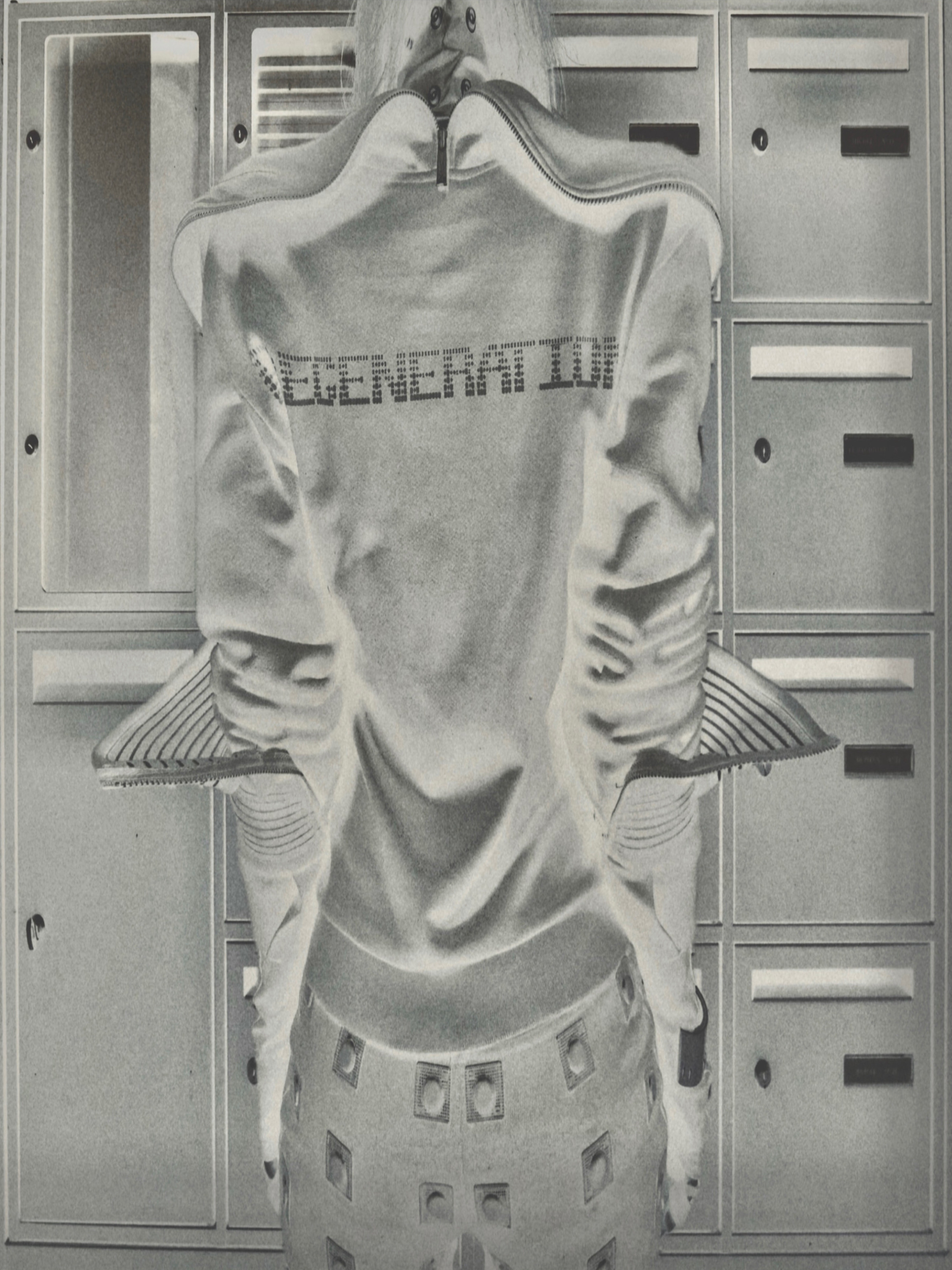 Spread from TheHunterIssue Vol.1 by Leo Shmunk, monochrome shot of a faceless figure in a white VETEMENTS tracksuit photographed from behind against a wall of mailboxes, gridded trousers below, 2026. Photo: Leo Shmunk.