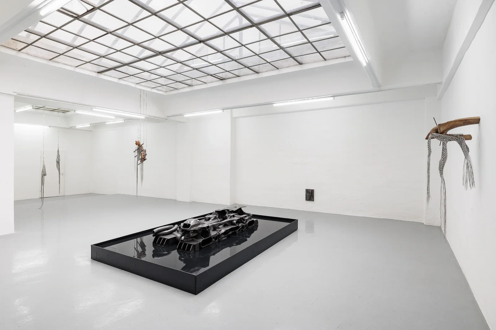 Installation view of NADIR at Gianni Manhattan, Vienna, with Laurence Sturla's graphite-patinated landscape resting in a black pool of water beneath the gridded skylight.