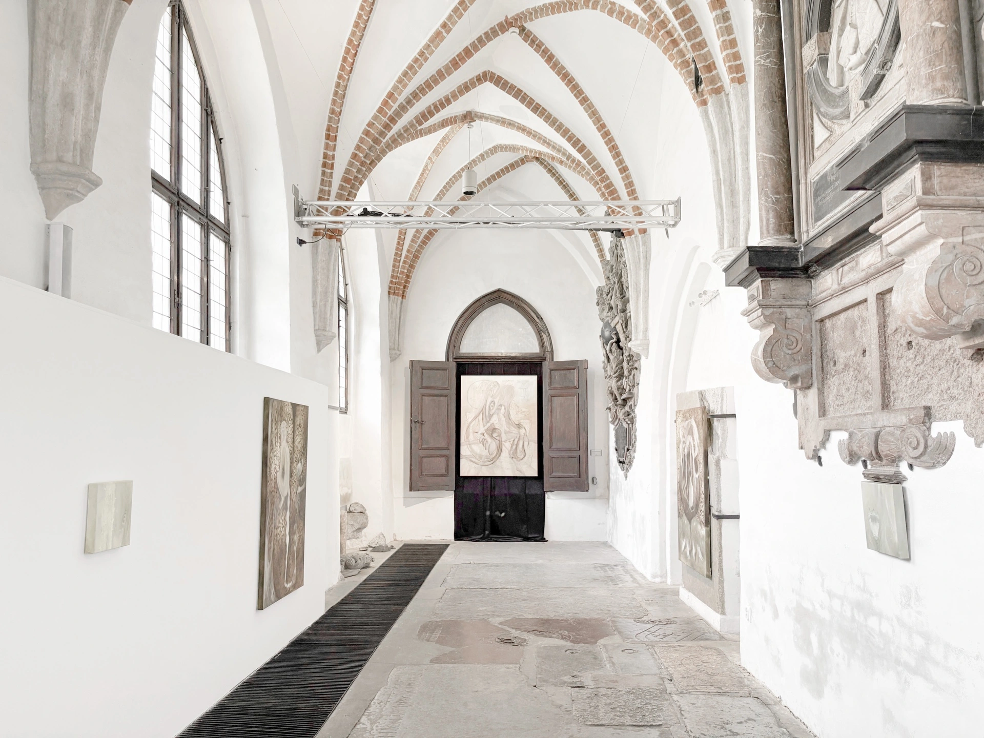 Installation view of Angelika Puff's Hairline at Galeria EL, a whitewashed Gothic church nave hung with pale paintings and sculptures of braided human hair draped across medieval tomb slabs.