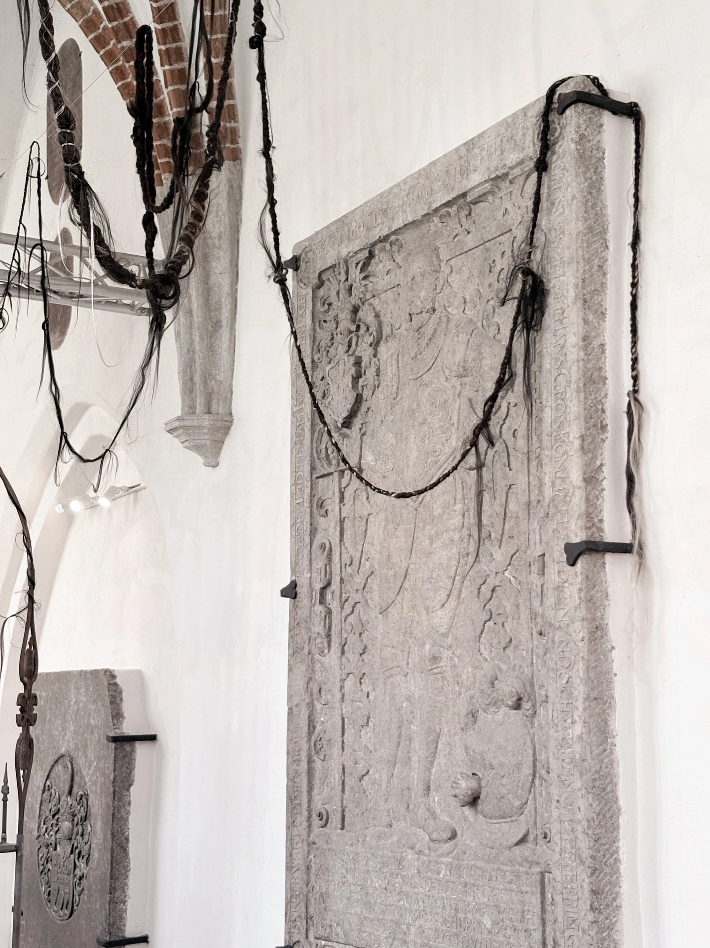 Angelika Puff, Bird Cage, chains of braided human hair draped across a carved medieval tomb slab suspended by iron brackets in Galeria EL.