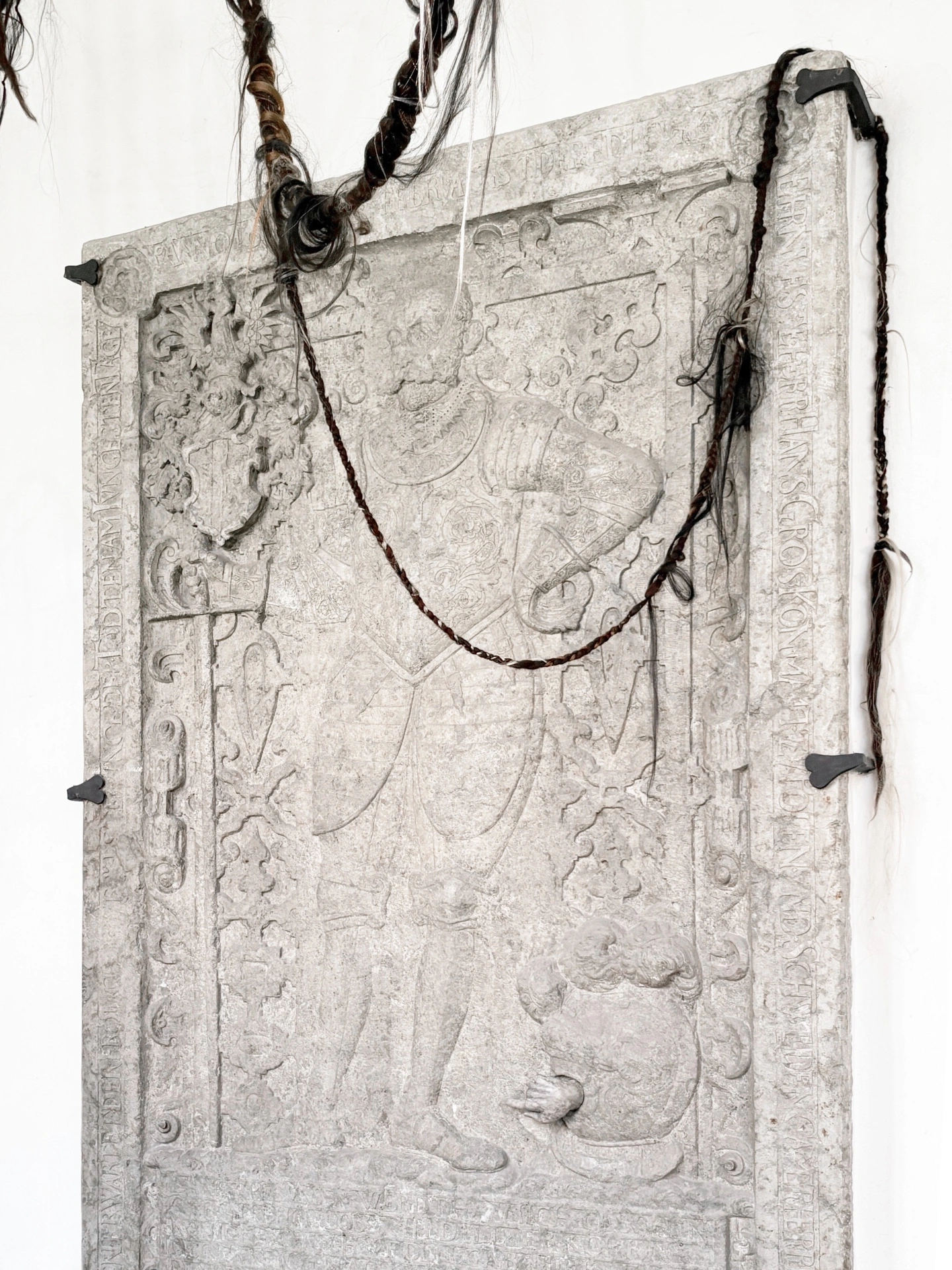 Angelika Puff, Bird Cage, 2025 — dark hair spilling through cage bars with Gothic brick arch and white plaster wall visible behind.