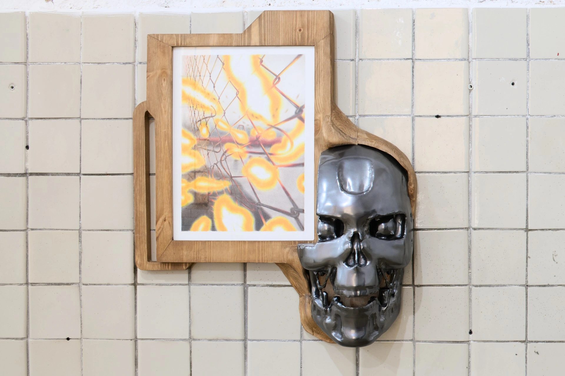 Tristan Gac, full Terminator endoskull in gunmetal beside a framed drawing of chain-link fence dissolving into yellow flame, white tile