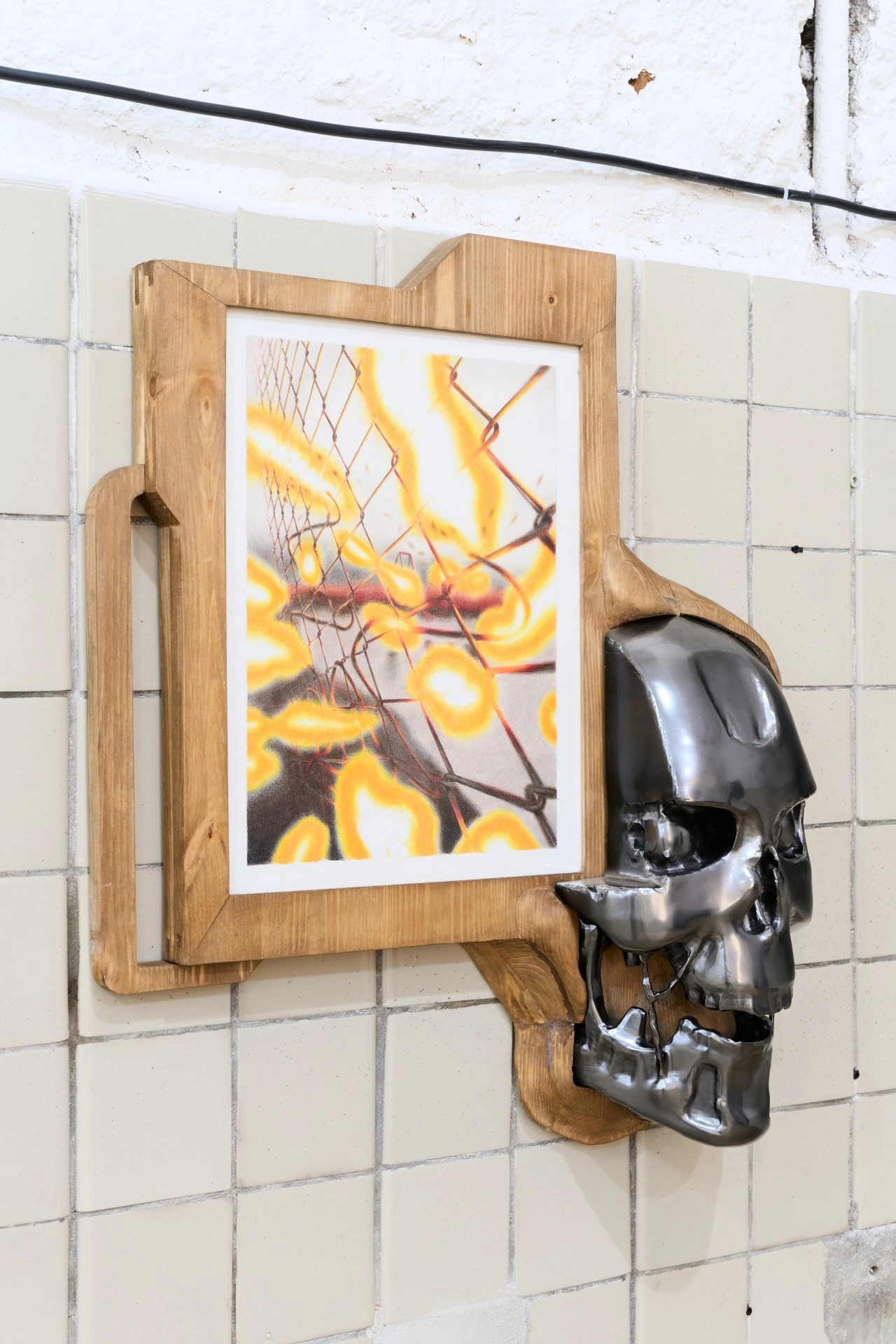 Tristan Gac, framed drawing of chain-link fence in yellow flame flares beside a chrome Terminator skull inlaid in pine, tiled wall