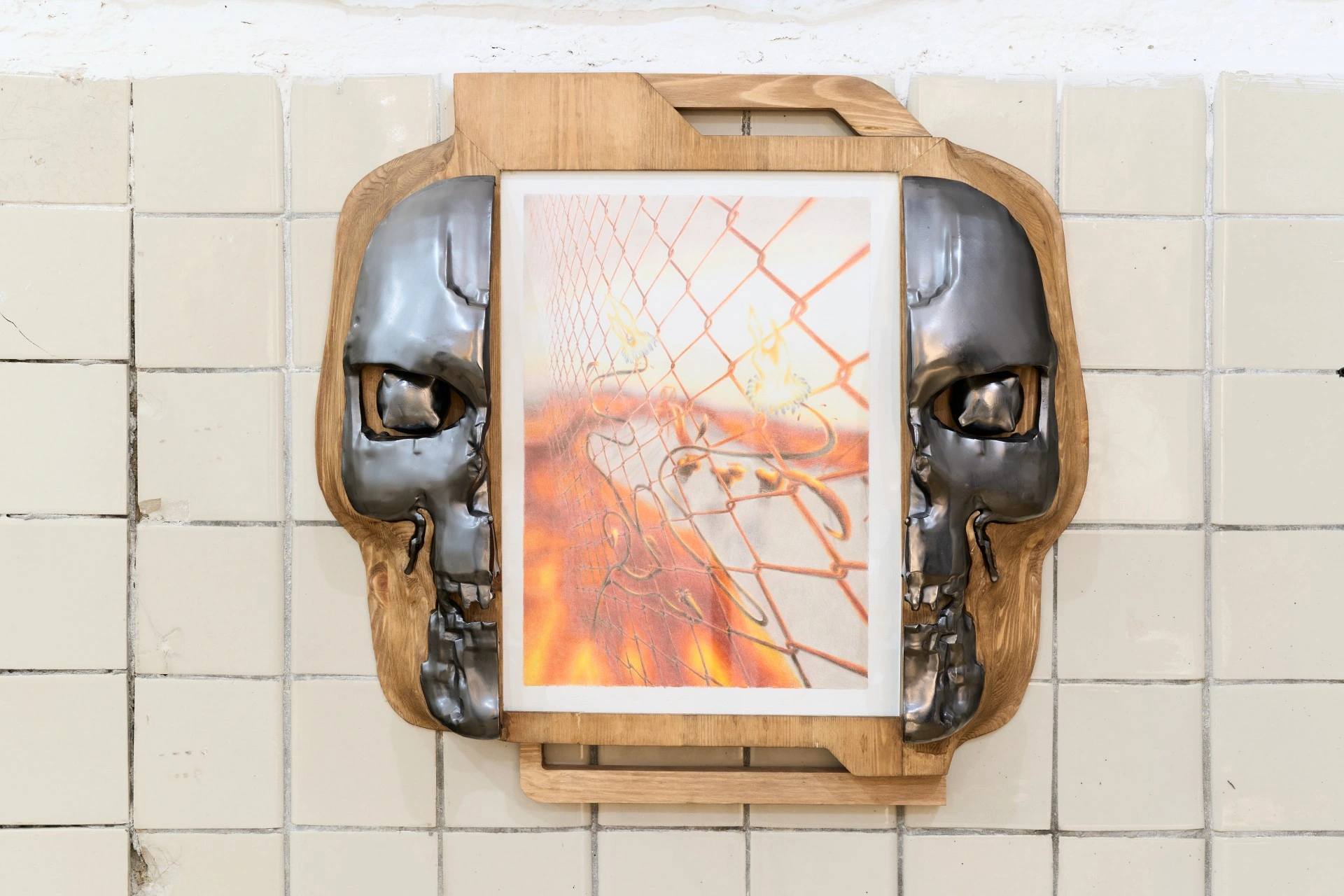 Tristan Gac, symmetrical work with a framed fire-and-fence drawing flanked by two mirrored gunmetal half-skulls set into pine, tiled wall