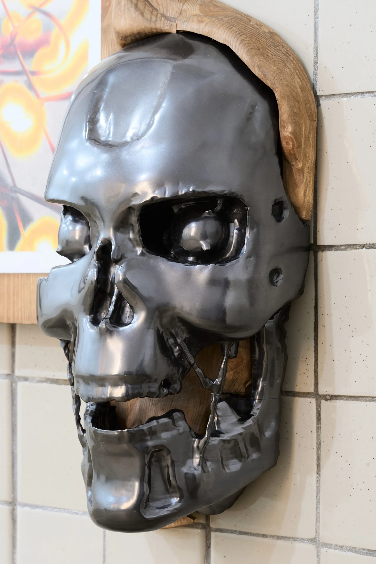 Tristan Gac, frontal detail of a polished gunmetal Terminator skull cracked at the jaw, cast into pine, framed fire drawing at left
