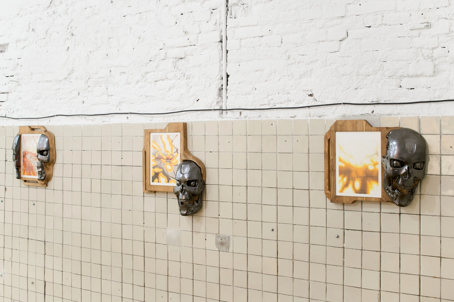 Tristan Gac, close row of Terminator endoskulls in gunmetal cast into pine brackets holding drawings of fence dissolving into orange fire