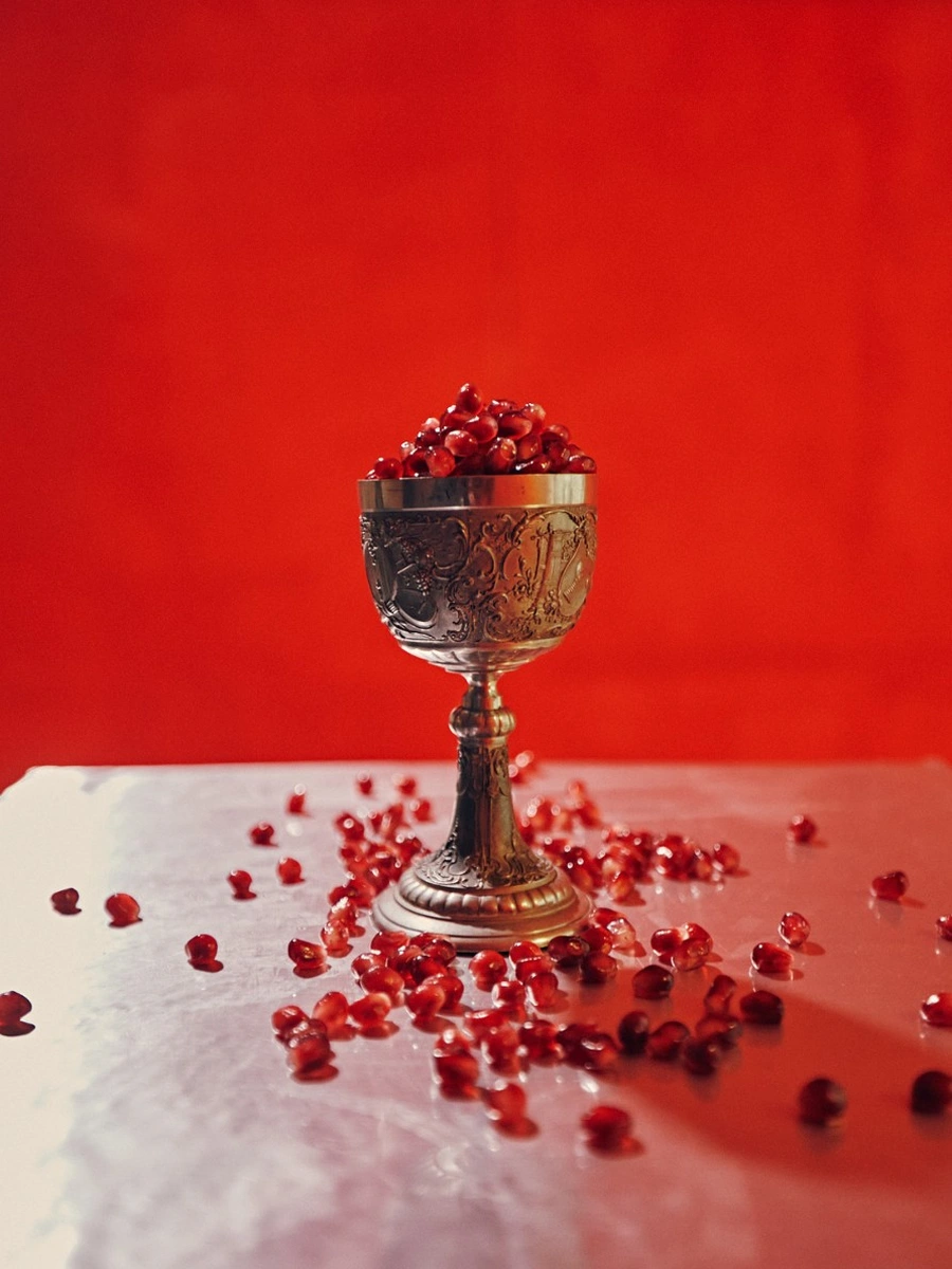 Still life detail, Seeds know no tree., New Fears Gallery, 2026: silver ornate chalice filled with pomegranate seeds on white marble surface, red background, scattered seeds. Photo: Sandro Mosco