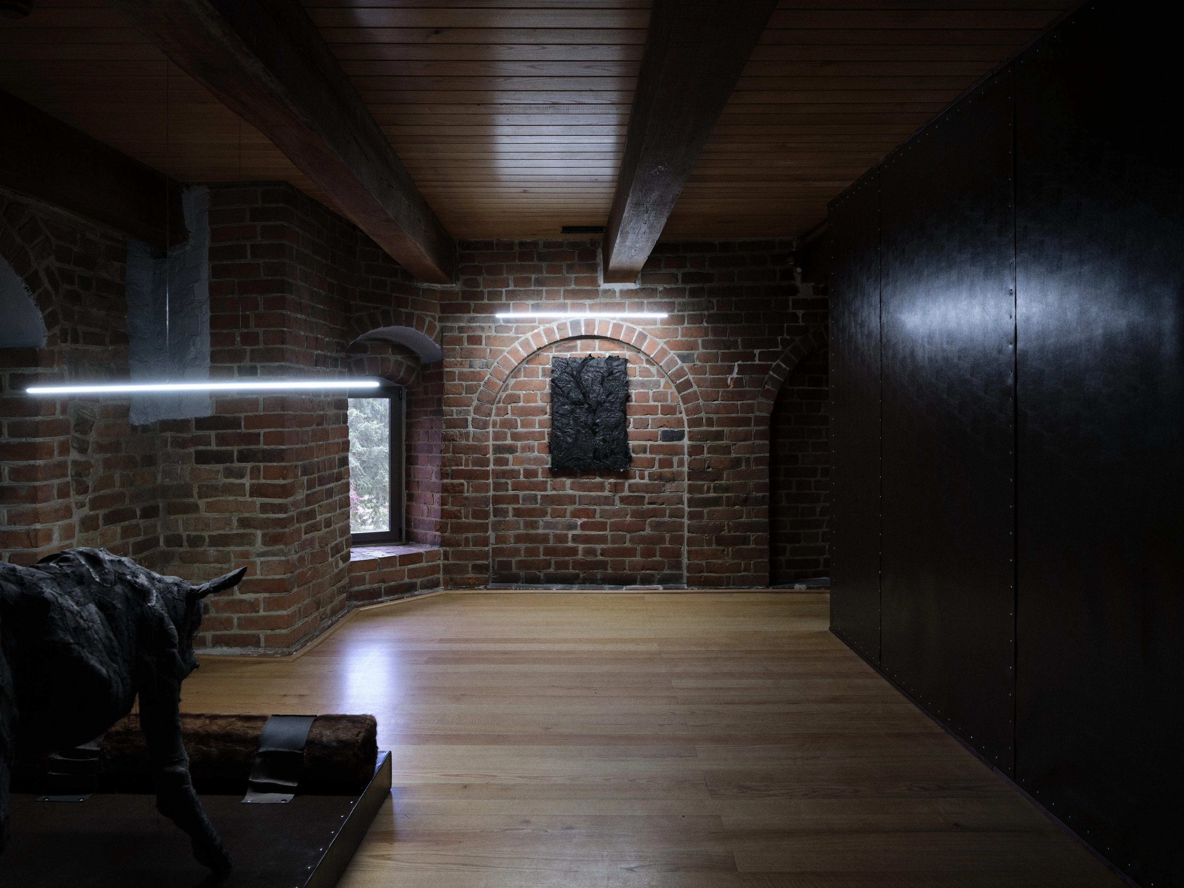 Jan Baszak's exhibition in a brick tower lined with dark faux leather: patched hide biers, a sock dog curled in a passage, a two-headed calf on a low platform and animal masks raised on metal stands.