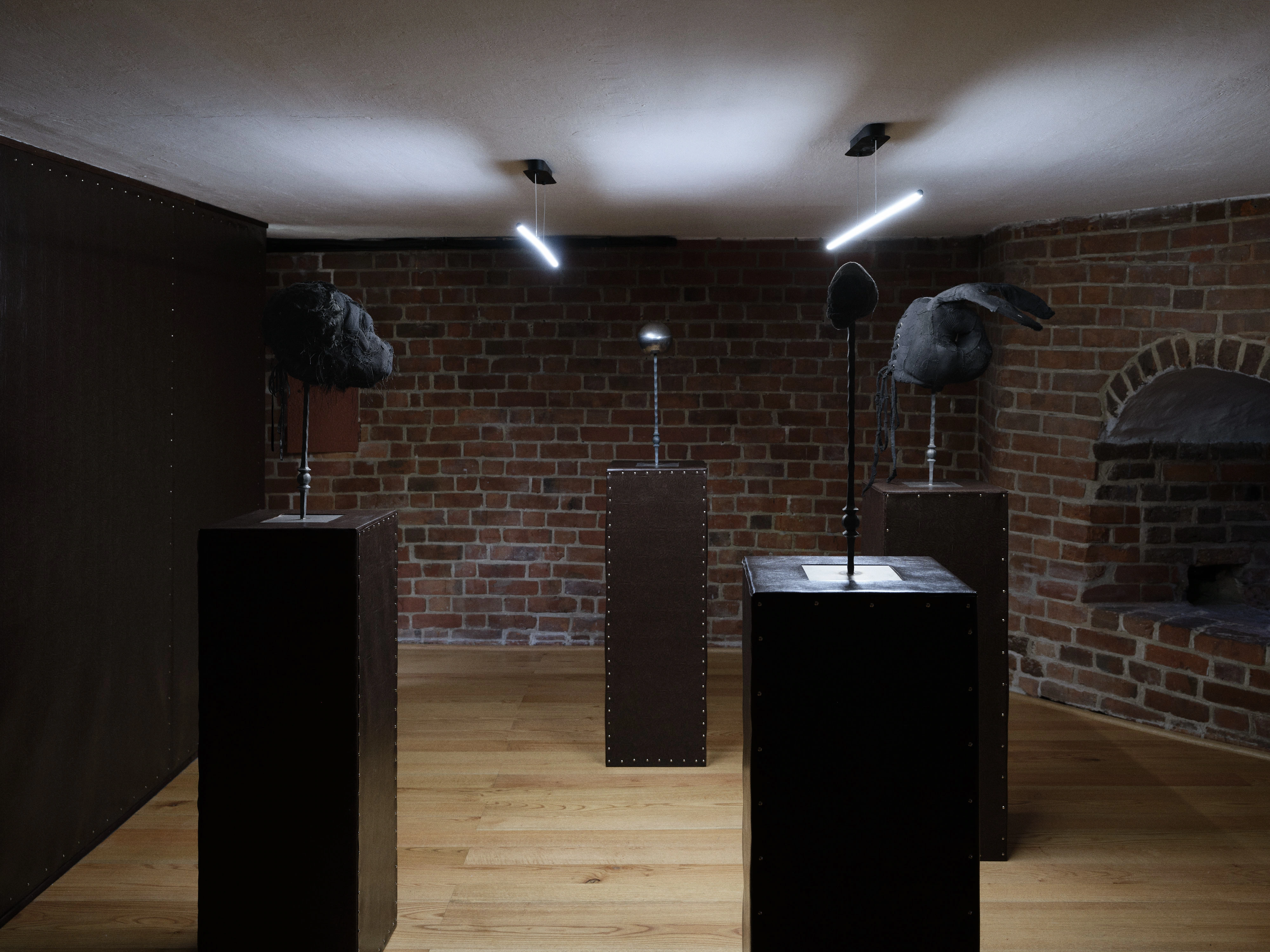 Jan Baszak, installation view of the mask floor with animal heads on metal stands atop faux leather plinths beneath two suspended light bars