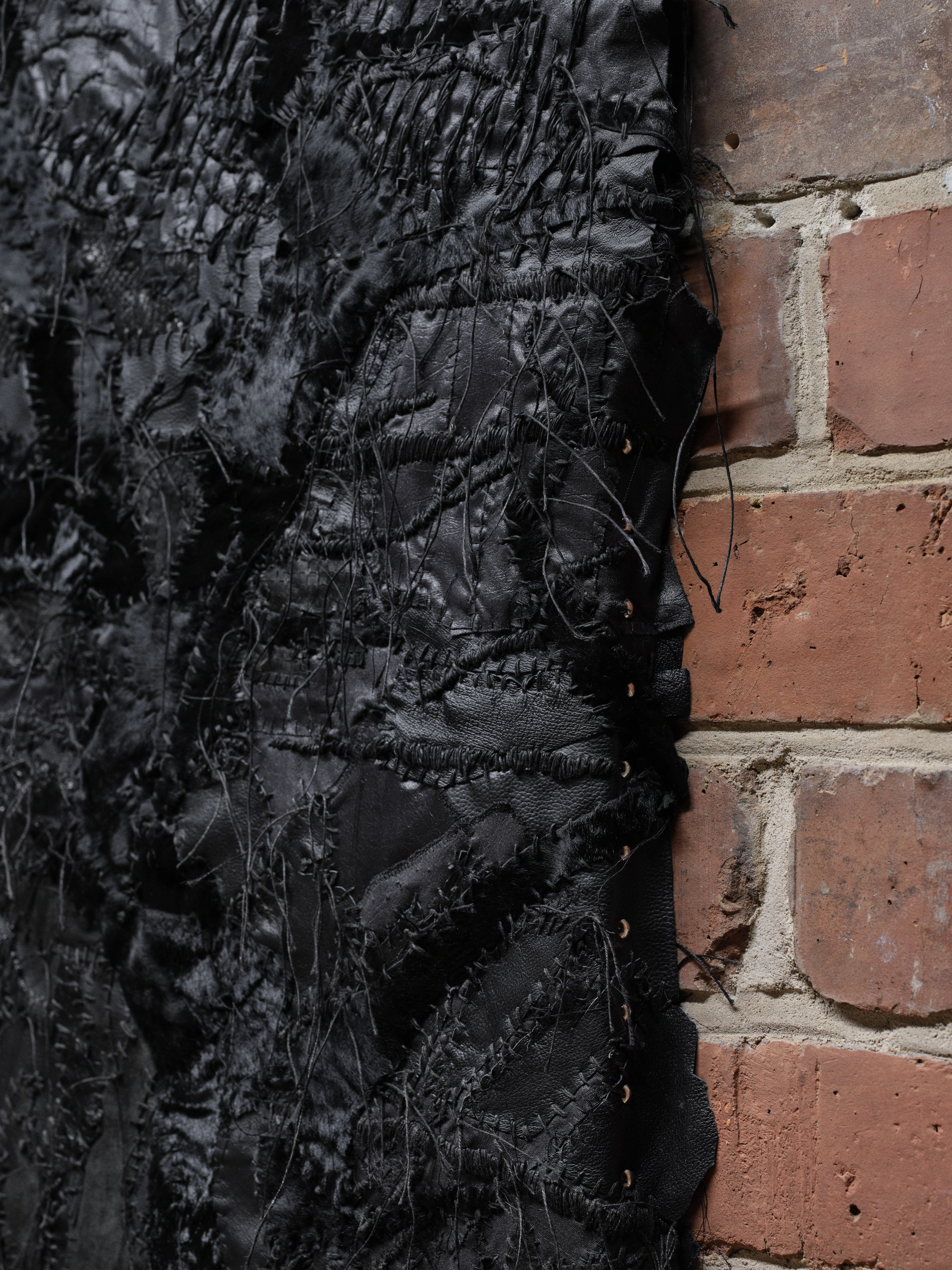 Jan Baszak, close detail of Tree of Crows where stitched black hide panels meet the brick wall, eyelets and stray threads along the edge