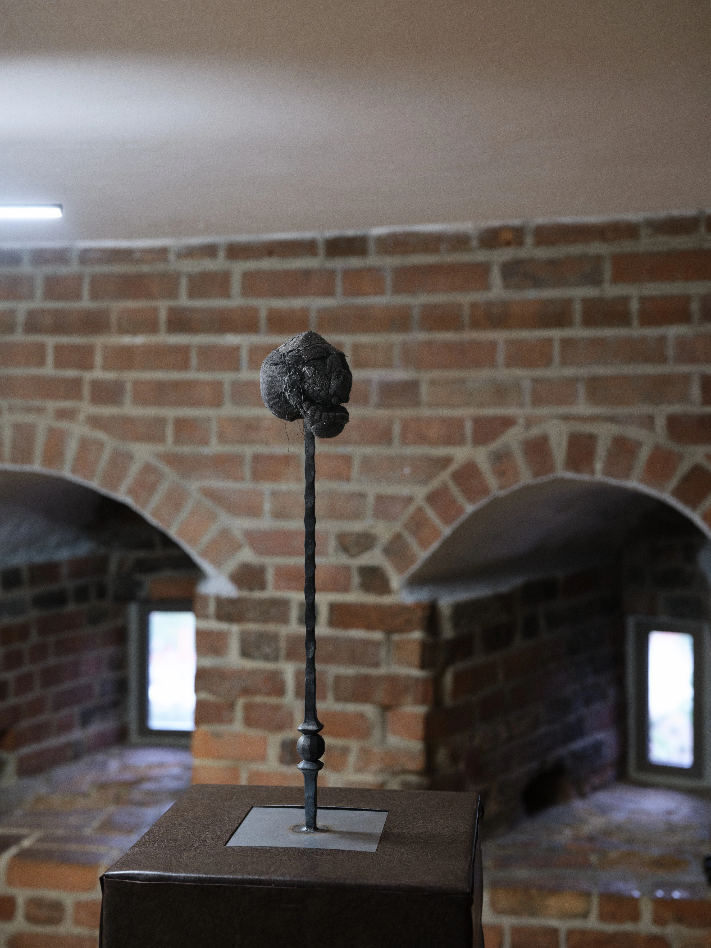 Jan Baszak, Laughing Head raised on a tall metal stand above a faux leather plinth, brick arches and window slits behind it